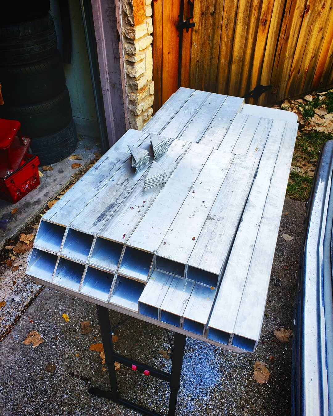 Cut and cleaned aluminum box section and flat bar laid out on a work table outside a shop