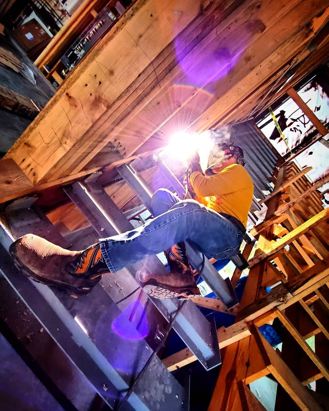 Welder burning rod on a set of cantilevered steel stair stringers inside a timber-framed build