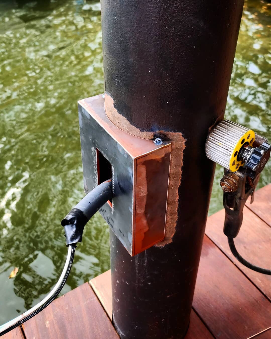 Custom steel outlet enclosure welded to a dock pier above green water