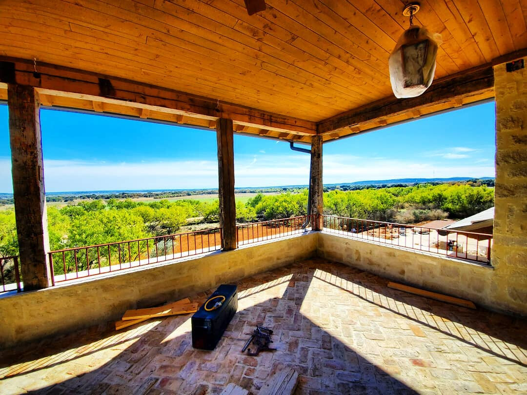 Covered stone porch with a steel guardrail overlooking hill country and Lake Buchanan
