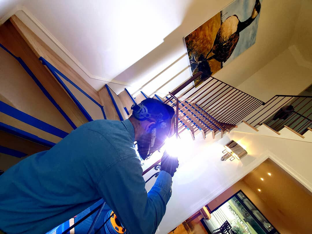 Welder welding a stair railing in place inside a finished home