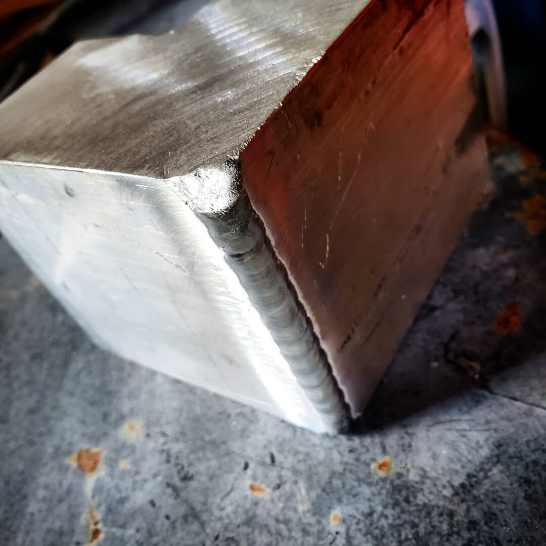 Close-up of a stacked-dimes weld bead joining an aluminum box section to steel plate